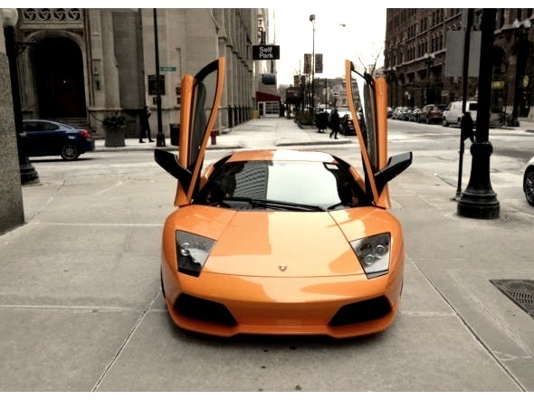 Orange Lamborgini Parked on Sidewalk With Doors upwww.DIscoverlavish.com